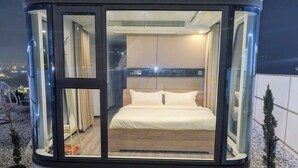 Un dormitorio moderno con paredes de vidrio, una cama, cortinas y vistas al cielo nocturno.