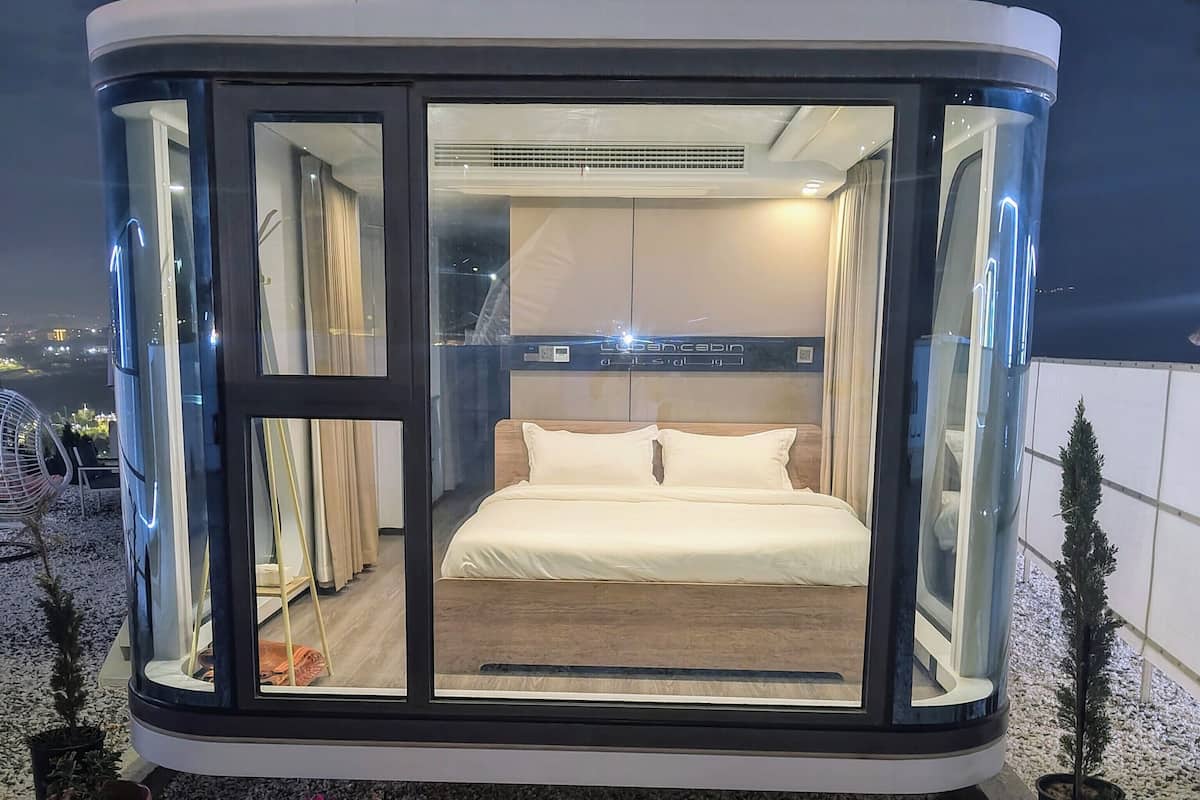 A modern, glass-walled bedroom with a bed, curtains, and a night sky view.