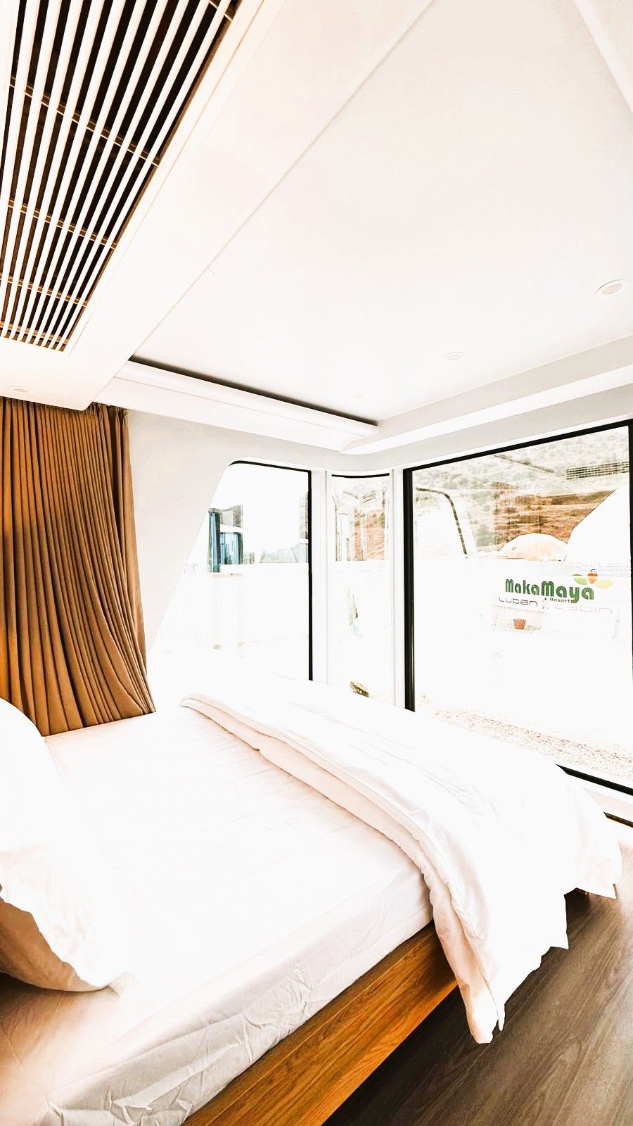 Une chambre moderne avec un grand lit, une fenêtre donnant sur un beau paysage et une bouche d’aération au plafond.