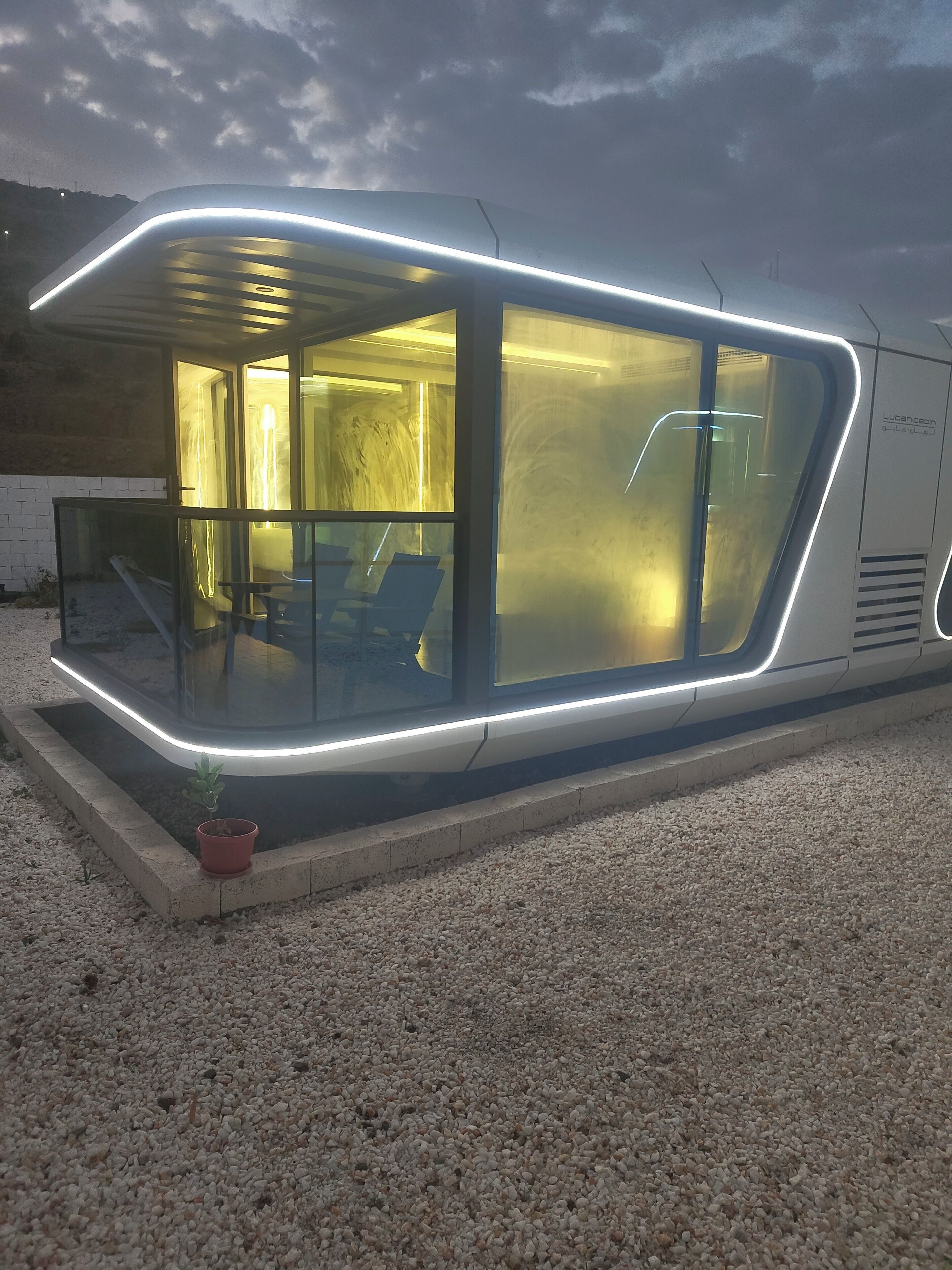 Un edificio moderno, iluminado, con amplios ventanales de vidrio y un área de descanso visible en su interior.