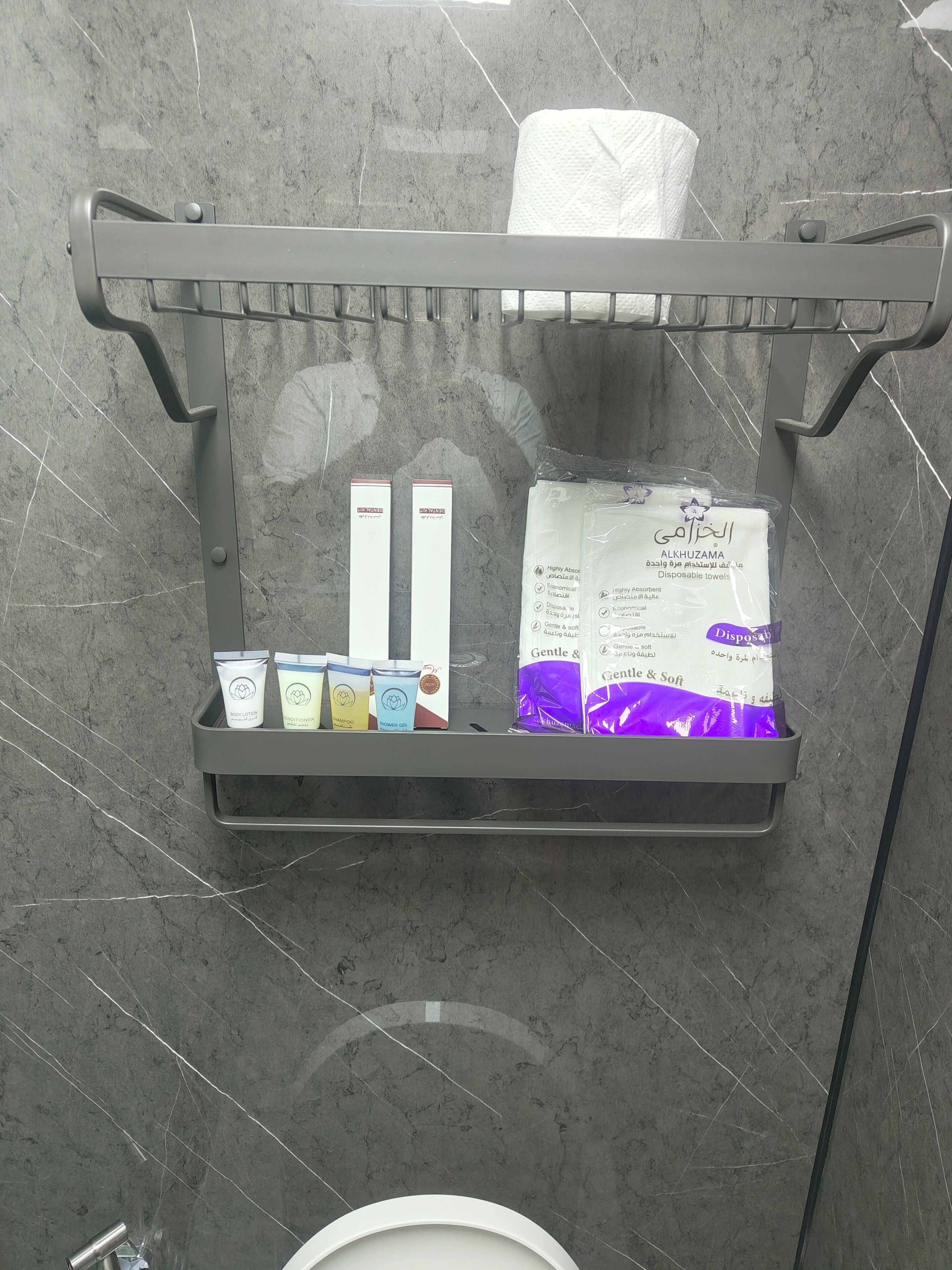 En hylla i badrummet med toalettartiklar, inklusive en näsdukask, ett paket med engångshanddukar och några personliga hygienprodukter.