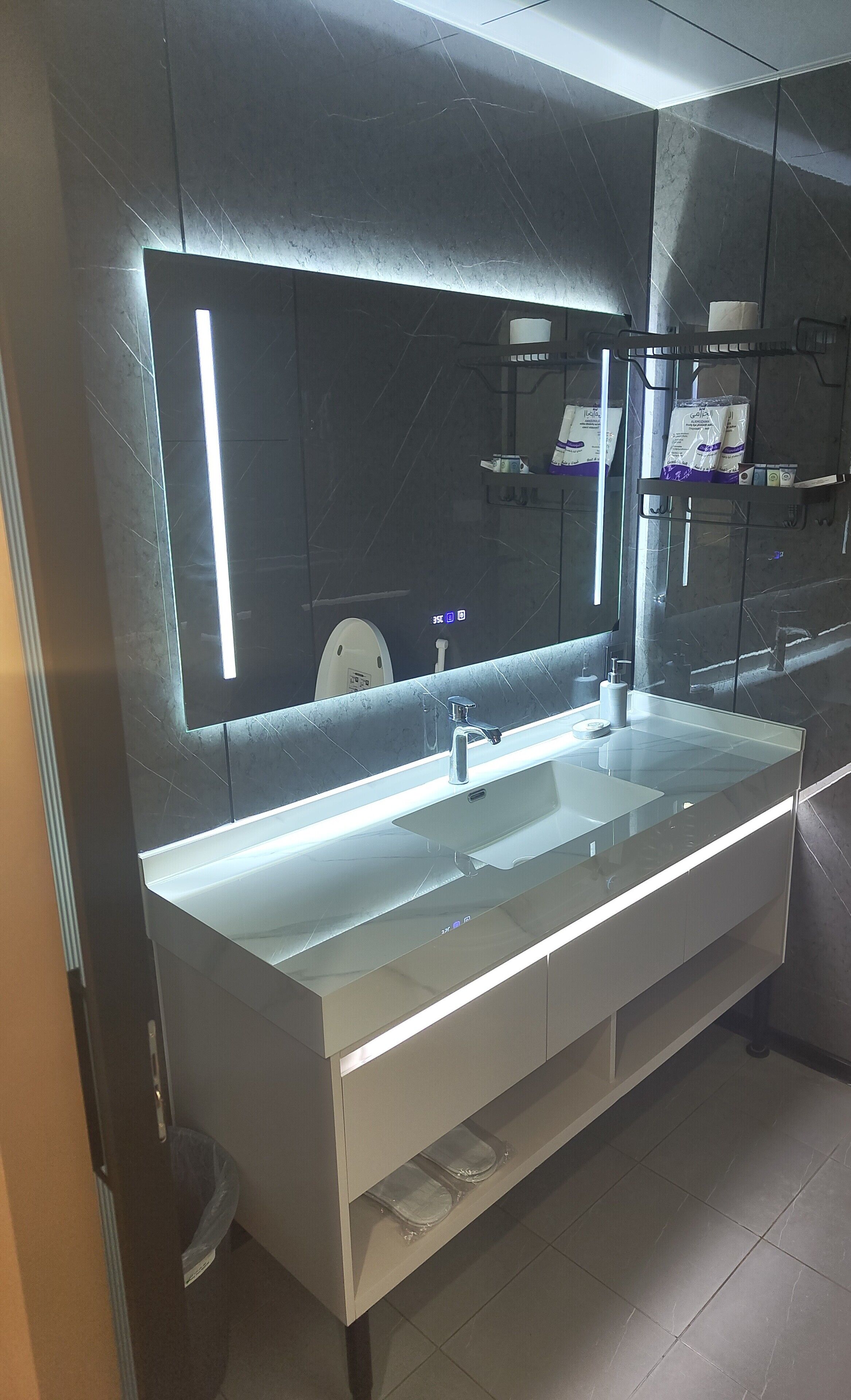 Un baño moderno con un espejo grande, un lavabo blanco y un perchero para toallas.