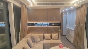 Una habitación de hotel moderna con un amplio sofá en forma de L, una mesa de centro redonda con un florero y un minibar.