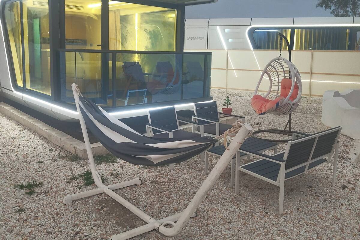 A modern, glass-enclosed structure with a seating area featuring a hammock and a swing chair.