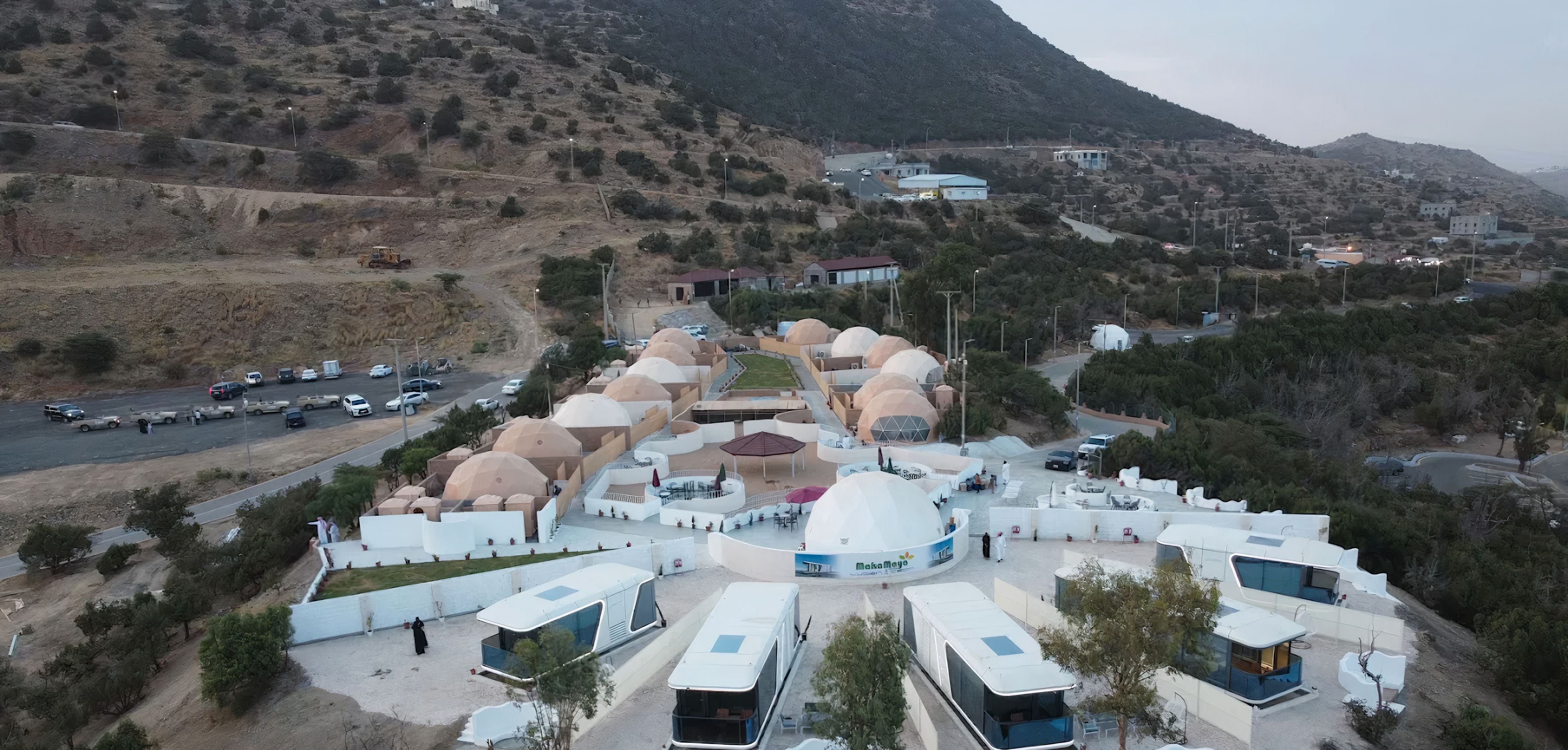 A modern resort with dome-shaped buildings, a central courtyard, and a mountainous backdrop.