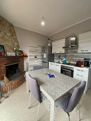 A modern kitchen with a stone fireplace, a dining table with chairs, and a built-in oven.