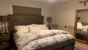 Ein Schlafzimmer mit einem hölzernen Bettgestell, floralem Bettbezug, Nachttischlampen und einem großen Spiegel.