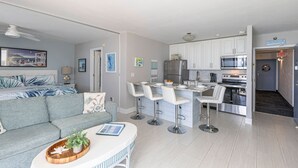 A modern kitchen with white cabinets, stainless steel appliances, and a bar area with white stools. - Estero Beach Tennis 1004c Direct Gulf Water Views (Fort Myers Beach)