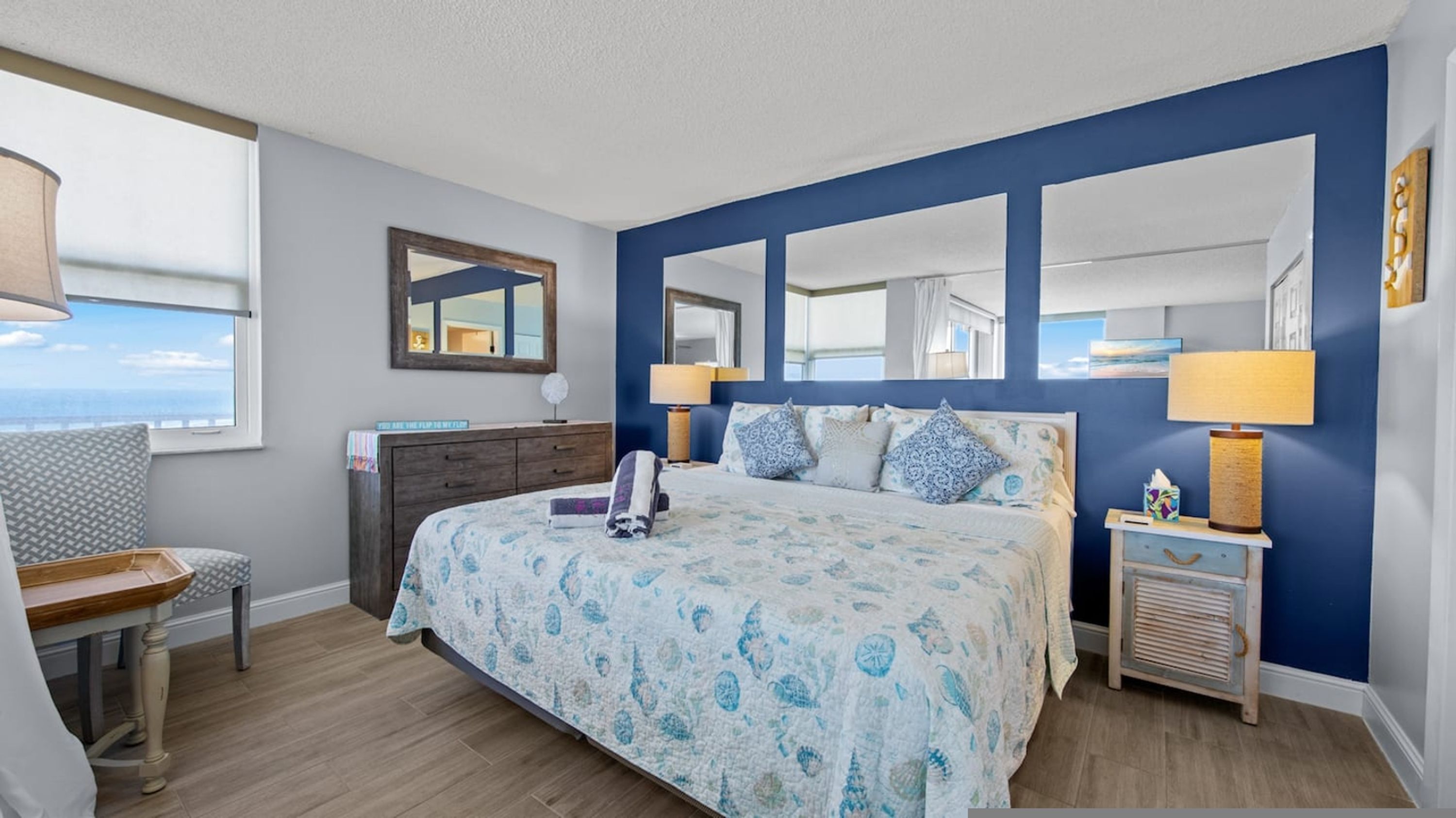 A bedroom with a bed, bedside tables, a chair, and a large window.