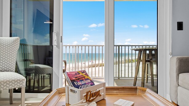 A room with a view of the beach, a wooden table, a chair, and a book titled "Vacation Guide".