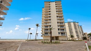 A high-rise hotel with multiple balconies, a beach view, and palm trees.