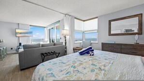 A modern hotel room with a large bed, a sofa, a desk, and a view of the ocean.