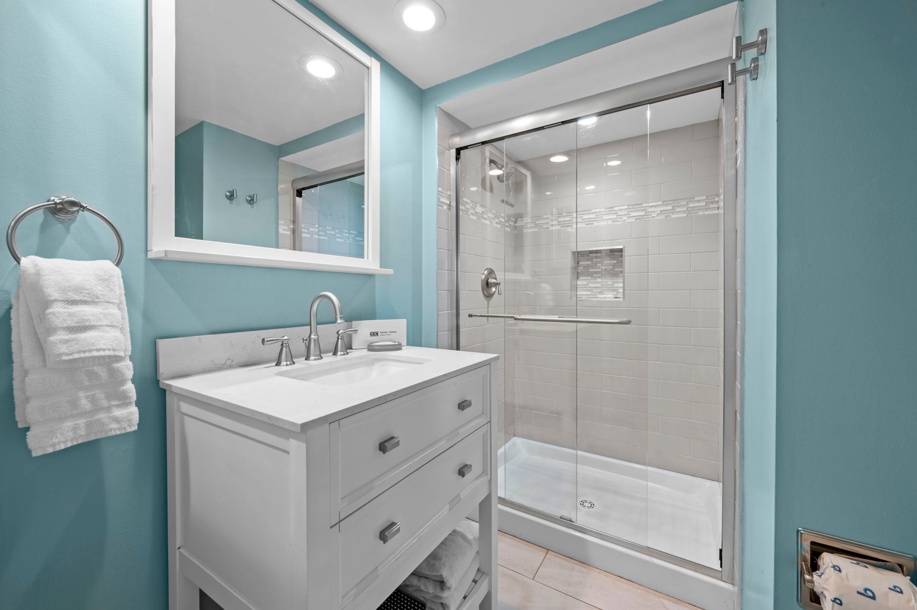 Une salle de bain avec un lavabo blanc, un miroir, une cabine de douche en verre et un porte-serviettes.
