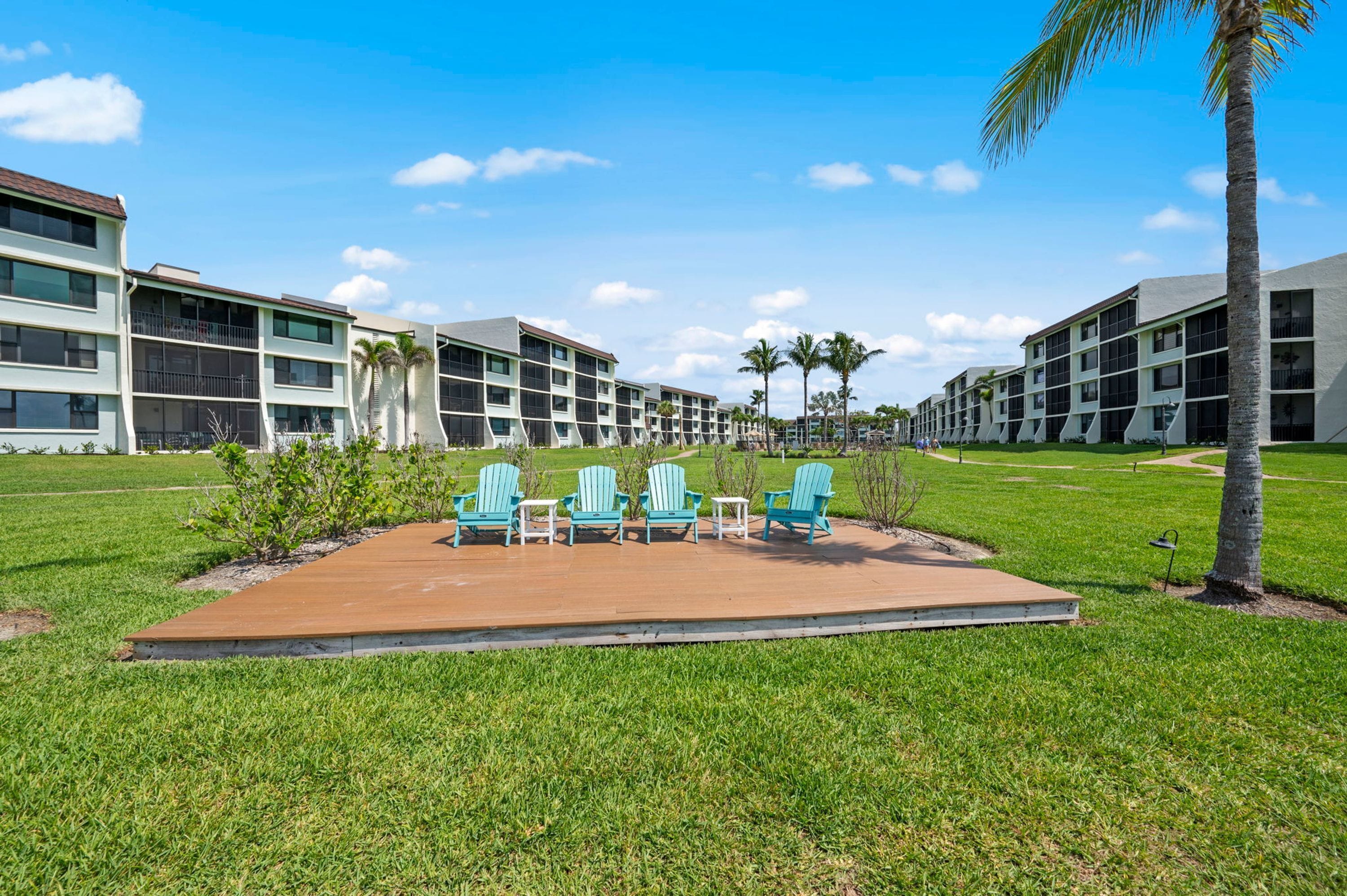 Un patio con mobiliario exterior, palmeras y un edificio con varios balcones.
