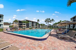 A swimming pool with lounge chairs and umbrellas, surrounded by palm trees and buildings. - Loggerhead Cay 302 w Bikes Pool on Beach (Sanibel)