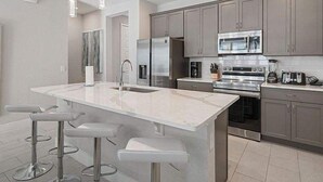 A modern kitchen with grey cabinets, stainless steel appliances, and a central island with bar stools.