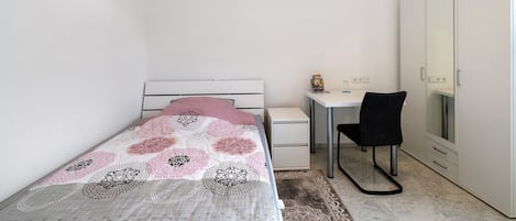 Une petite chambre avec un lit, un bureau, une chaise et une armoire.