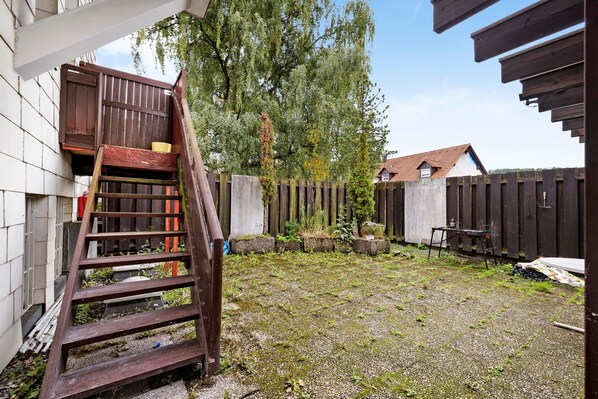 A backyard with a wooden staircase, a wooden fence, and a building in the background.
