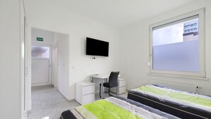 Un dormitorio con cama, escritorio, silla, televisor y ventana.