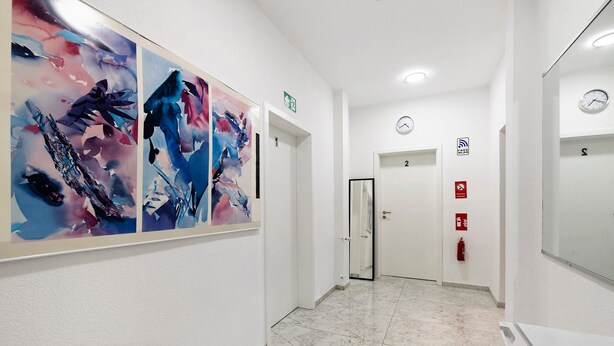 Un pasillo con arte abstracto en las paredes, puertas numeradas, un reloj y un extintor.