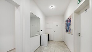 Un pasillo con paredes blancas, un refrigerador, un bote de basura y una puerta con un número.