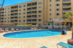 Ein Swimmingpool mit Liegestühlen und ein mehrstöckiges Gebäude im Hintergrund.