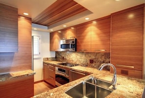 Eine moderne Küche mit Holzschränken, Granit-Arbeitsplatten, Edelstahlgeräten und Einbauleuchten.