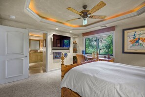 Un dormitorio con cama, ventilador de techo, ventana con vistas y puerta que da a un baño.