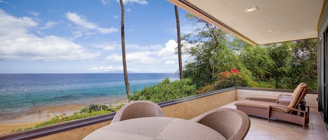 A balcony with wicker furniture overlooking a beach and ocean.
