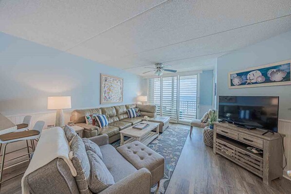 A living room with a sofa, coffee table, TV stand, and artwork on the walls. - 402 Southpoint in Ponce Inlet, FL (Ponce Inlet)