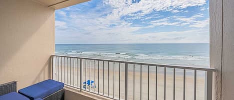 A balcony with a view of the beach, featuring a railing and seating area.