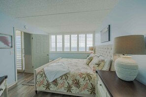 A bedroom with a bed, a nightstand, a lamp, and a window with blinds. - 402 Southpoint in Ponce Inlet, FL (Ponce Inlet)