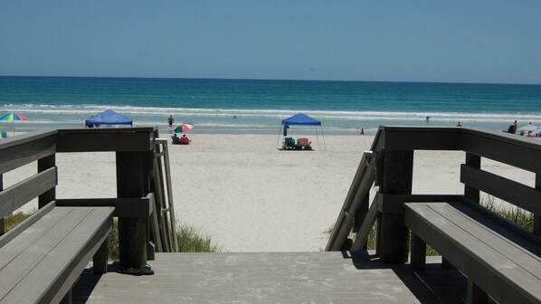 Een houten looppad dat naar een strand leidt, met parasols en ligstoelen.