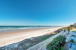 A beach view with a paved walkway, seating area, and a railing. - #402 Southpoint 2/2 Oceanfront Traffic Free Beach (Ponce Inlet)