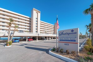 A hotel with a signboard indicating weekly and monthly rentals, a parking area with several cars, and a clear blue sky. - #402 Southpoint 2/2 Oceanfront Traffic Free Beach (Ponce Inlet)
