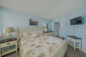 A bedroom with a bed, nightstands, a television, and a painting on the wall. - #402 Southpoint 2/2 Oceanfront Traffic Free Beach (Ponce Inlet)