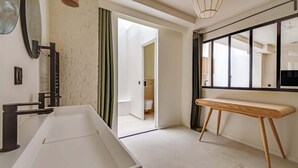 Ein modernes Badezimmer mit einer großen Badewanne, einer Holzbank und einem Fenster mit schwarzen Rahmen.