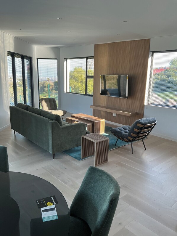 A modern living room with a sofa, chairs, a coffee table, and a TV mounted on a wooden panel. - Enjoy a relaxing getaway in our new luxury apartment, central to most amenities (Cape Town)