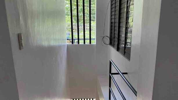 A staircase with a metal handrail, a black and white patterned wall, and a window with vertical bars.