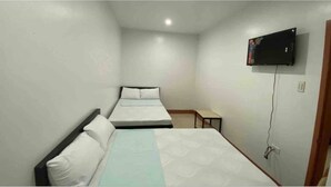 A small, clean room with two single beds, a TV mounted on the wall, and a small table.