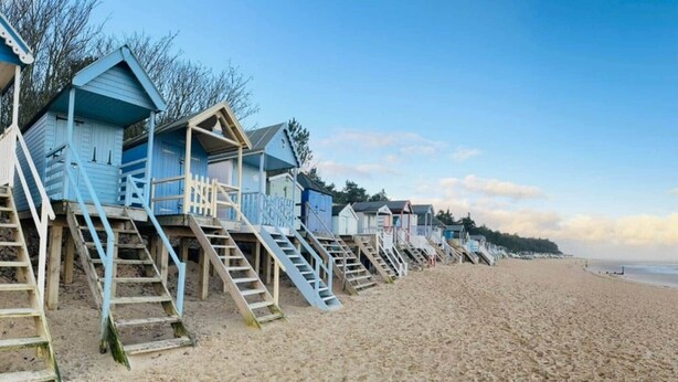 A row of beach huts with wooden stairs leading up to them, situated on a sandy beach. - Blakeney. Harbour View (Blakeney)