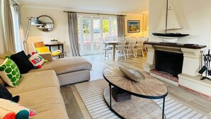 A living room with a sofa, a round coffee table, a fireplace, and a dining area with chairs and a table. - Blakeney. Harbour View (Blakeney)