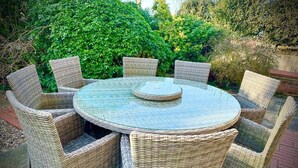 A round wicker table with six chairs, set outdoors with a brick floor and greenery in the background. - Blakeney. Harbour View (Blakeney)