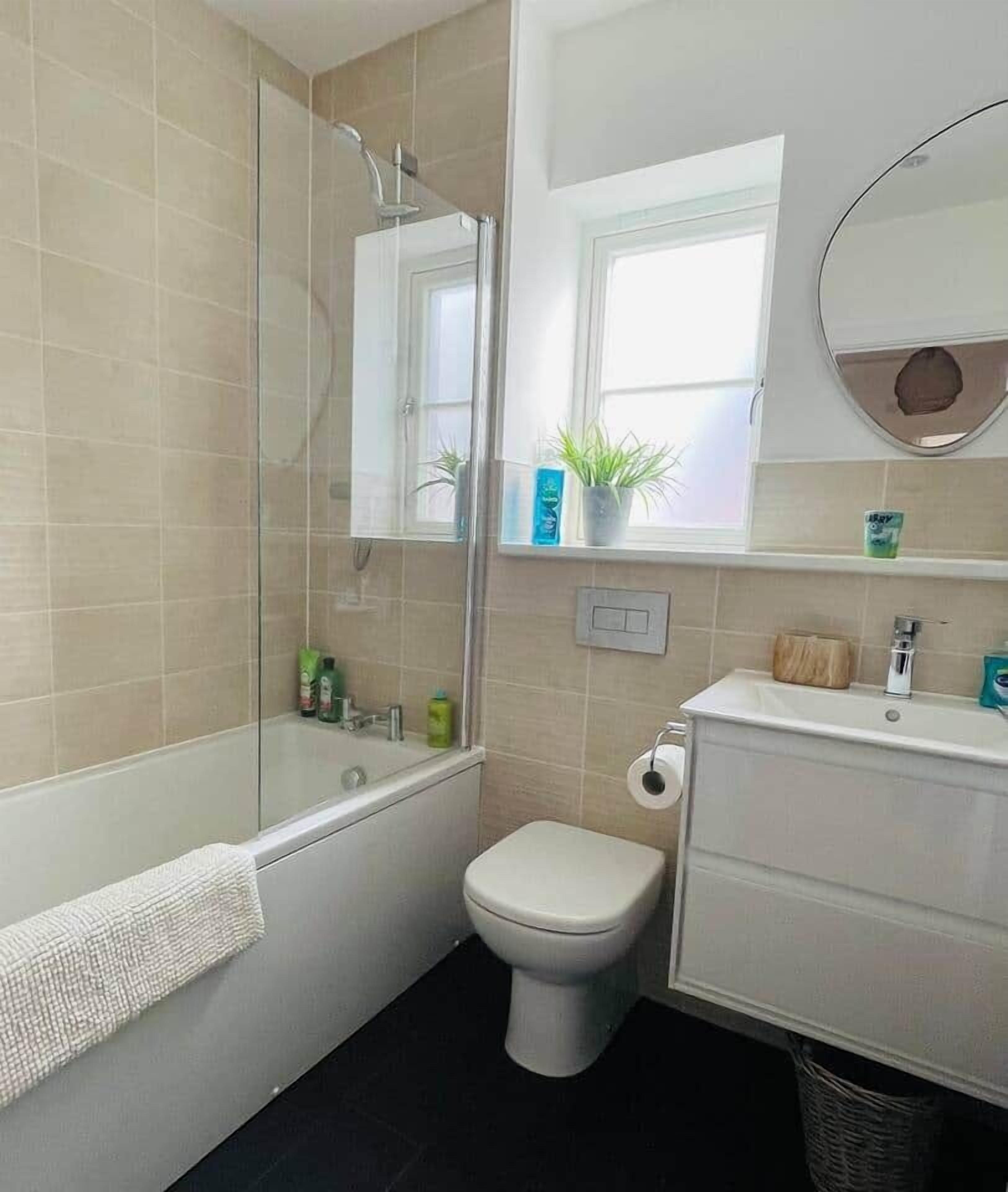 A bathroom with a bathtub, toilet, and sink. There is a window with a plant on the windowsill.