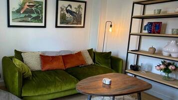 A living room with a green sofa, a round wooden coffee table, and a bookshelf with decorative items.