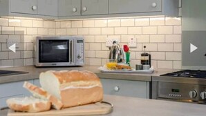 A kitchen with grey cabinets, a microwave, a gas stove, and a loaf of bread on the counter. - West Cottage. Central, spacious, 2 mins to beach. (Cromer)