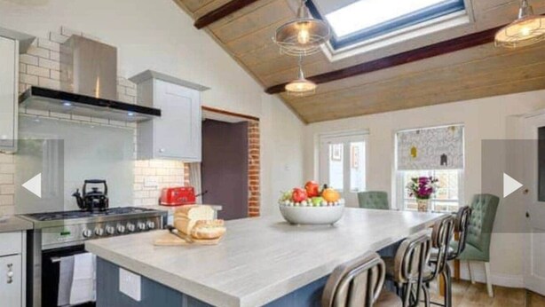 A modern kitchen with a central island, a gas stove, and a brick wall. - West Cottage. Central, spacious, 2 mins to beach. (Cromer)