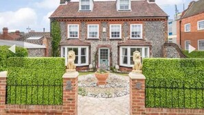 A two-story house with a brick facade, multiple windows, and a front garden with a statue. - West Cottage. Central, spacious, 2 mins to beach. (Cromer)