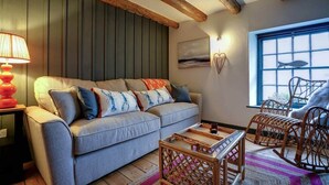 Een gezellige woonkamer met een grijze bank, houten balken, een houten salontafel en rieten stoelen.