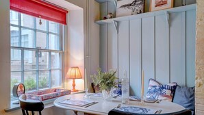 Een eetgedeelte met een ronde tafel, stoelen, een raam met rode gordijnen, een lamp en een plank met ingelijste foto's.